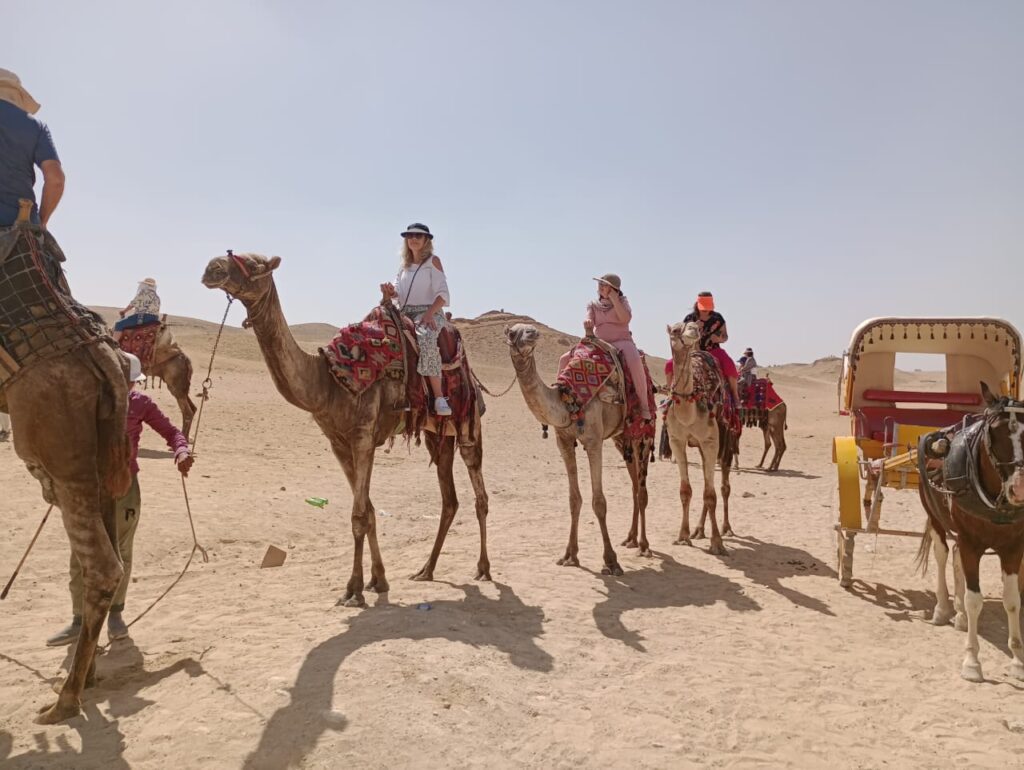 Grupo de turistas em um passeio de camelo no deserto do Egito, próximo às pirâmides, uma atividade divertida e segura em uma viagem em grupo.