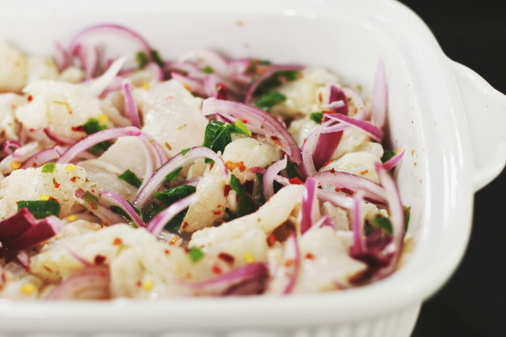 Close-up de um prato de ceviche com pedaços de peixe branco marinado em limão, cebola roxa fatiada e pimenta, um prato típico da gastronomia peruana.