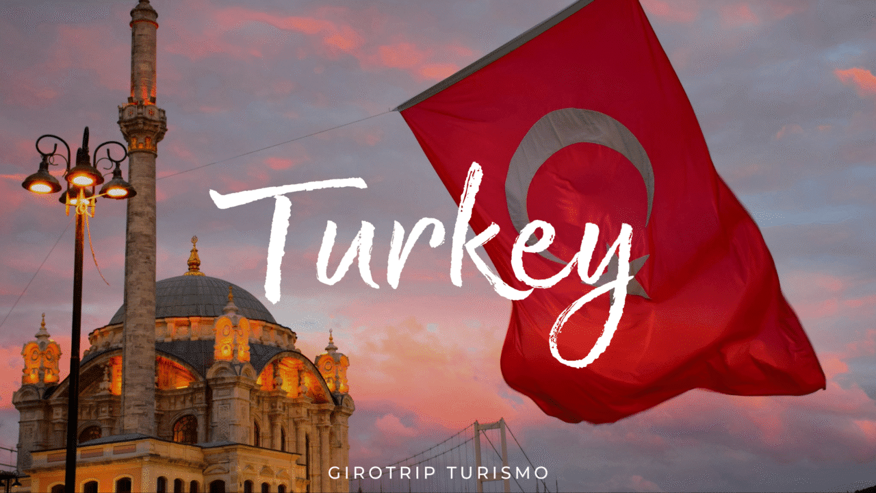 Imagem de capa para o artigo "Visitar a Turquia: Quando Ir, o Que Não Perder." mostrando a Mesquita Ortaköy ao pôr do sol com a bandeira da Turquia em primeiro plano. Logotipo da Girotrip Turismo na parte inferior.