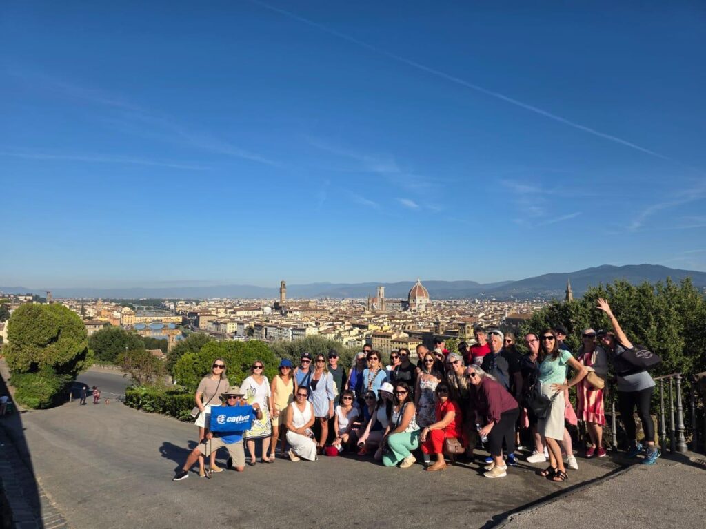 Um grupo de viagem da Girotrip posando para uma foto com vista panorâmica da cidade de Florença, Itália, em um dia de sol.