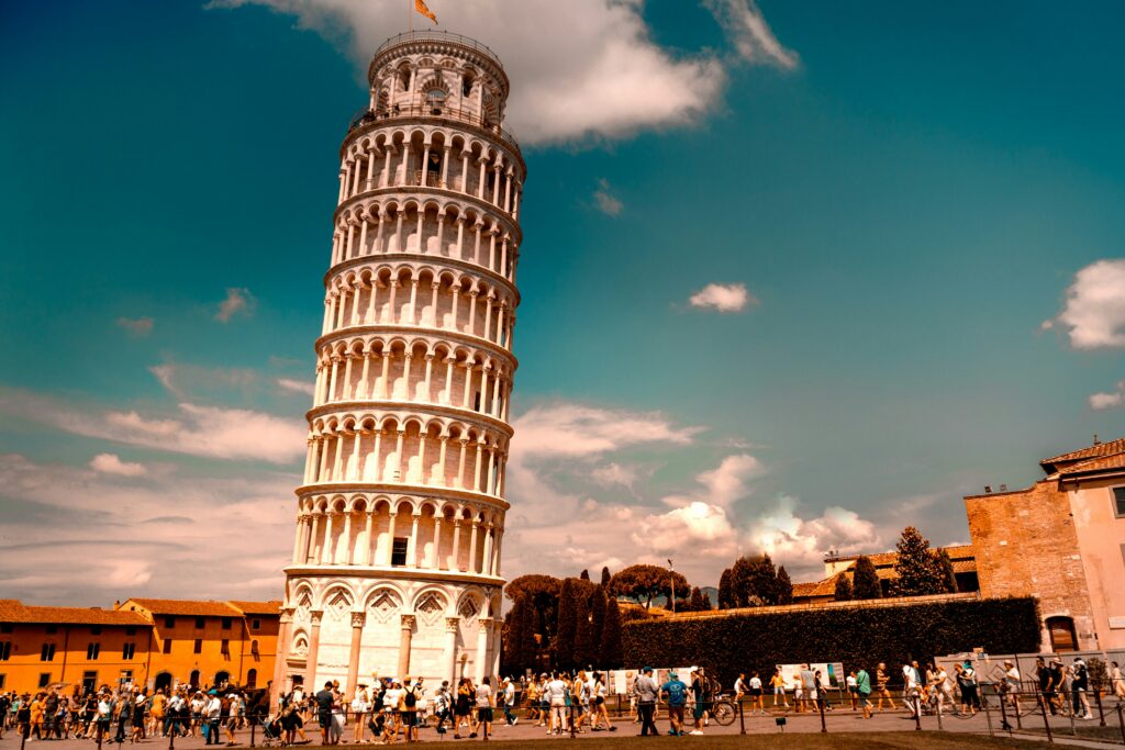 A famosa Torre Inclinada de Pisa em um dia ensolarado, cercada por turistas, um destino clássico para uma viagem em grupo na Itália.