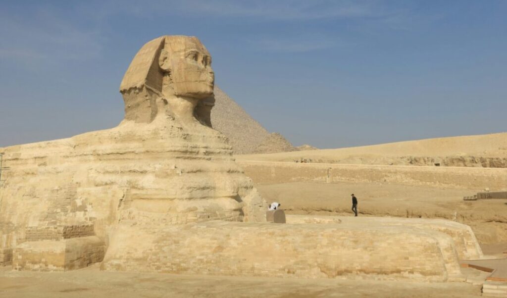 A monumental Grande Esfinge de Gizé no Egito, com uma pirâmide ao fundo no deserto, um ponto turístico imperdível na sua viagem em grupo.