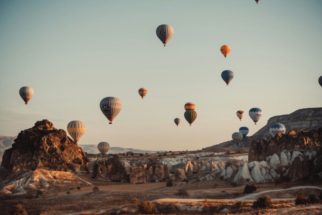 Centenas de balões de ar quente voando sobre as formações rochosas únicas da Capadócia ao nascer do sol, um passeio imperdível em uma viagem em grupo para a Turquia.